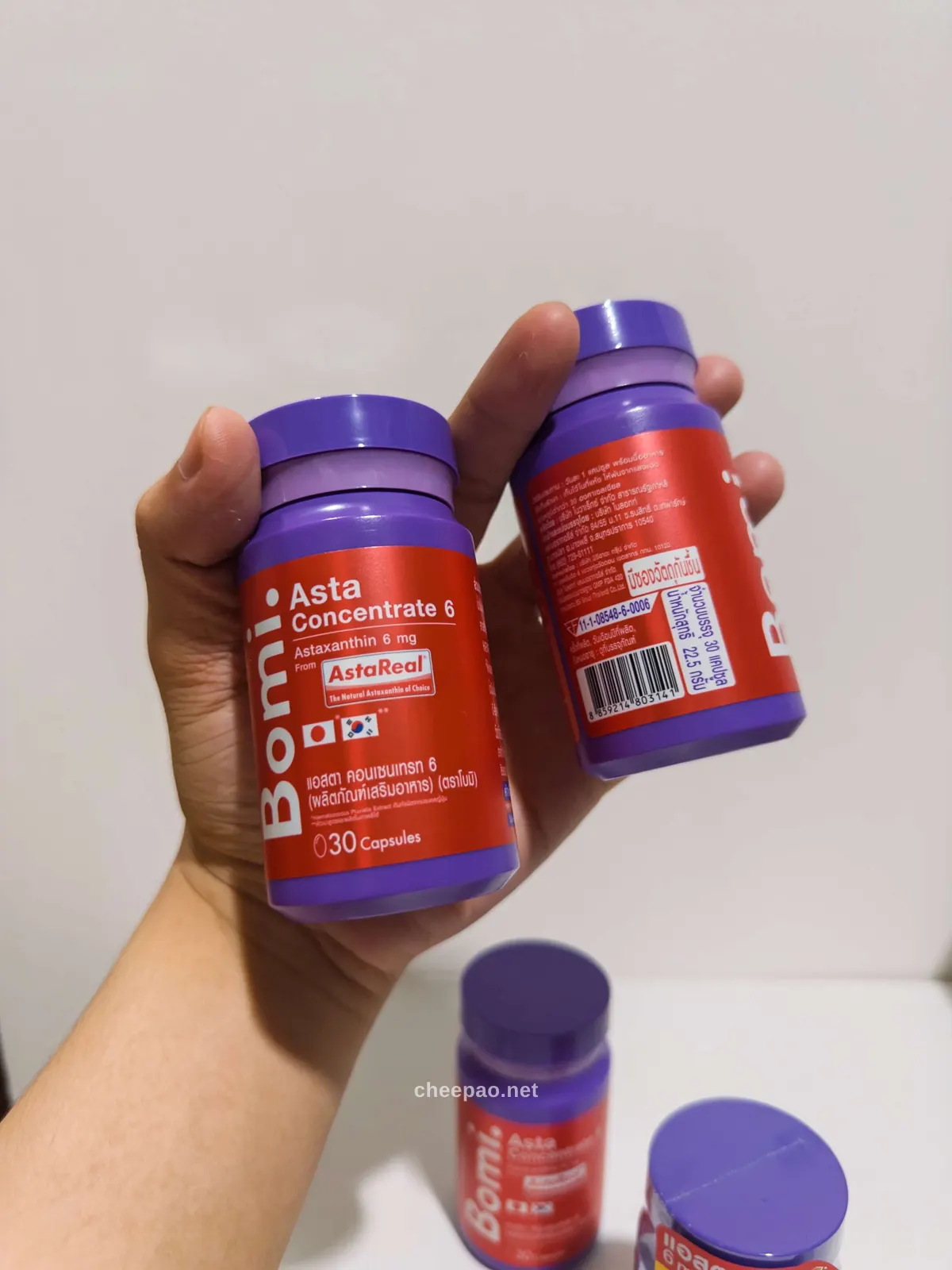 มือถือขวด Bomi Asta Concentrate 6 สองขวด เห็นฉลากด้านหน้าและด้านหลังพร้อมเลขทะเบียน อย.